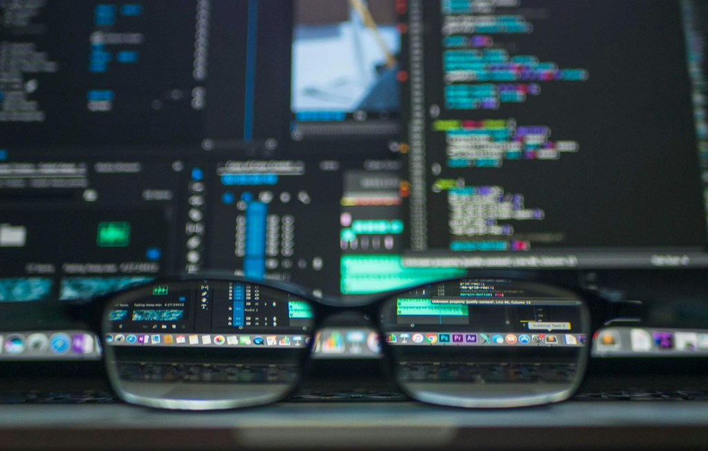 A pair of glasses sitting in front of a computer monitor displaying code.